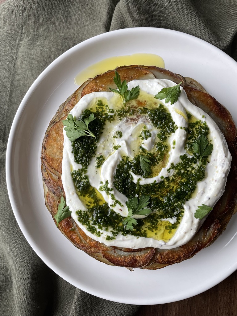 Golden potato cake with white yogurt sauce, green chive vinaigrette and parsley on a white plate.