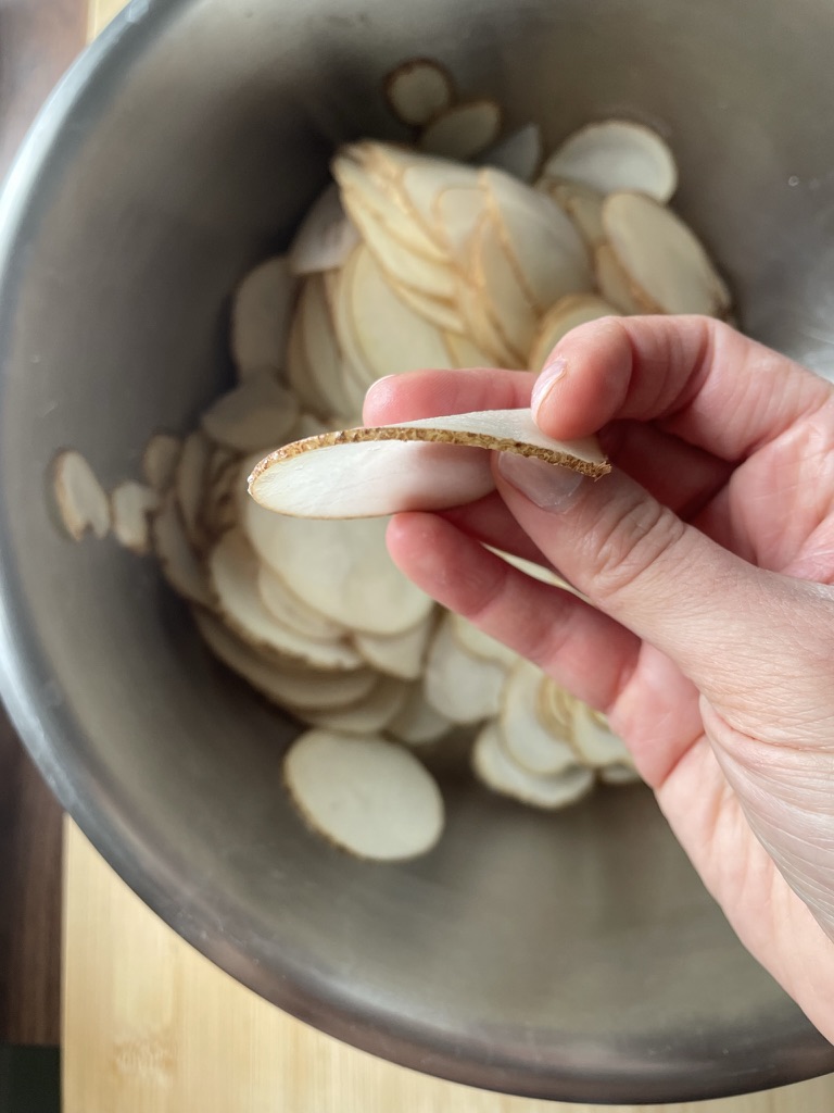 Hand holding a thinly sliced potato for visual example of thickness.