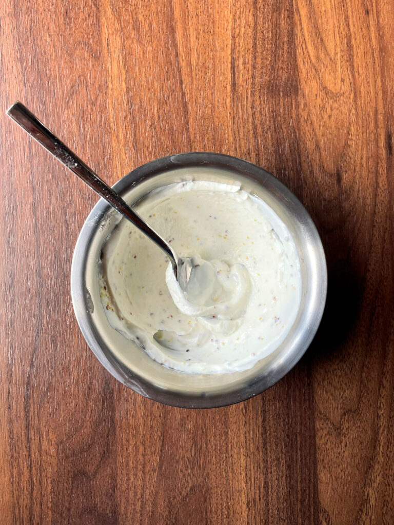 Creamy yogurt sauce speckled with grainy mustard in a stainless steel bowl.