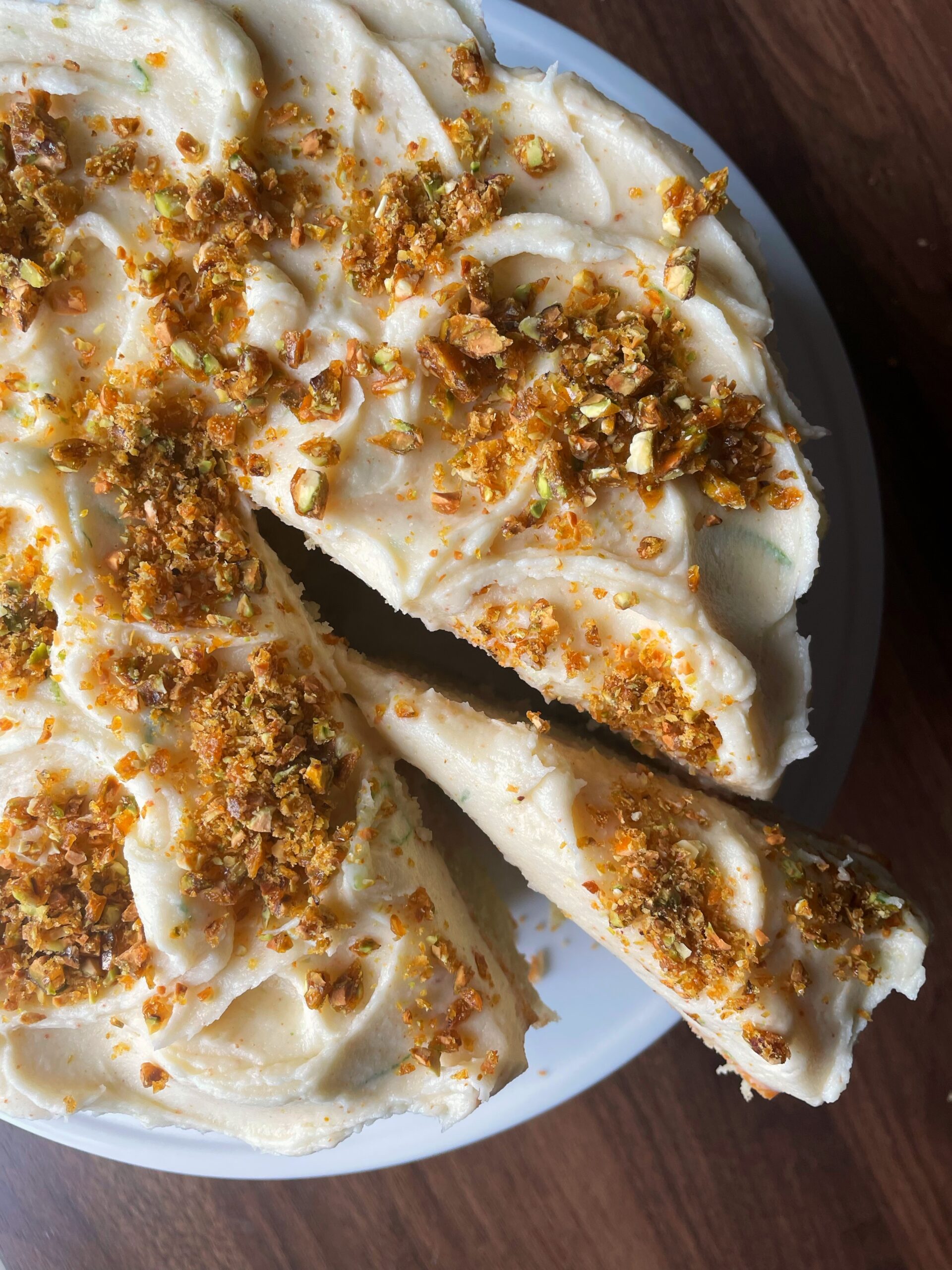 Top view of a cake with white frosting and crumble on a white stand with a wooden background.