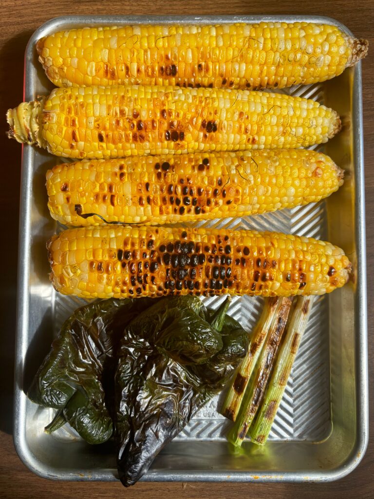 Charred poblano peppers, scallions and corn on a quarter sheet pan.