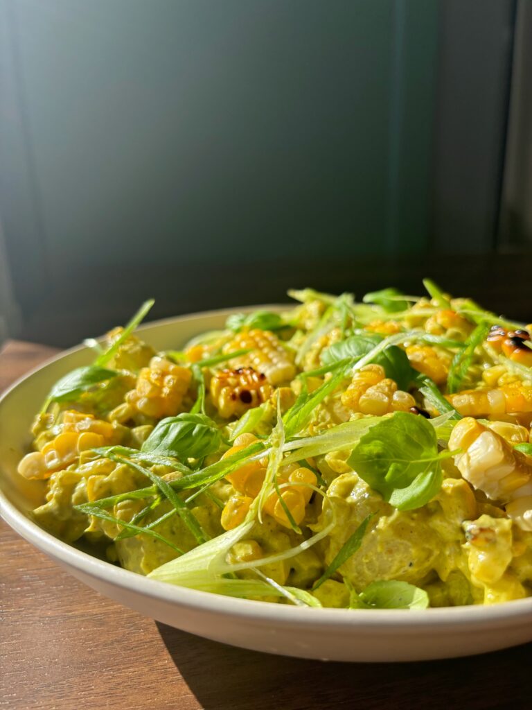 Close up photo of potato, corn and poblano salad with scallions scattered on top on a wooden table with a green background.