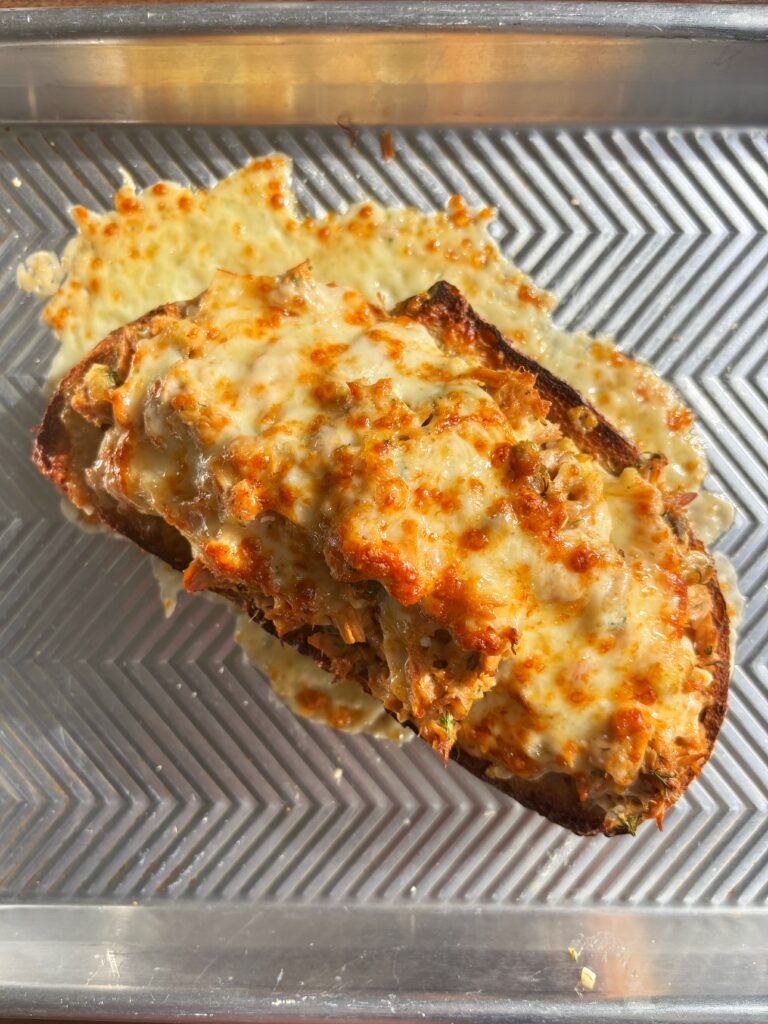 Tuna melt with golden and crispy cheese on a metal sheet pan.