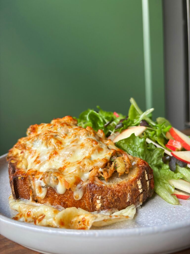 Bread with tuna salad and melted cheese beside a green salad on a large grey plate with a green background.