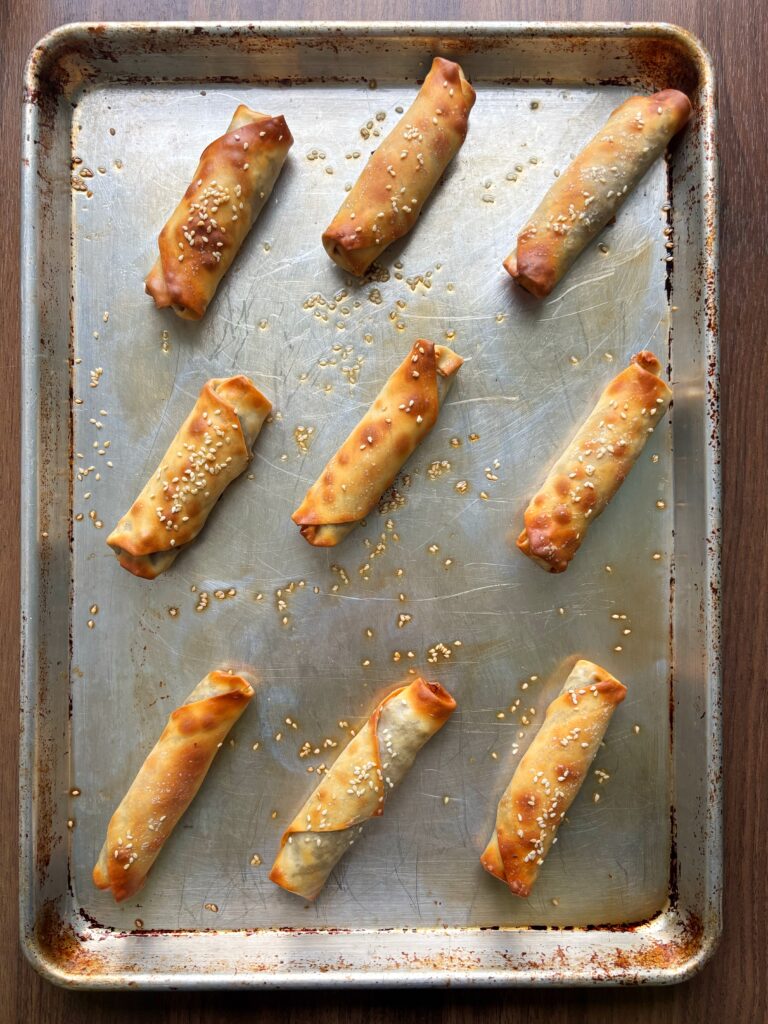 Nine Tourtiere spring rolls on a metal sheet pan.