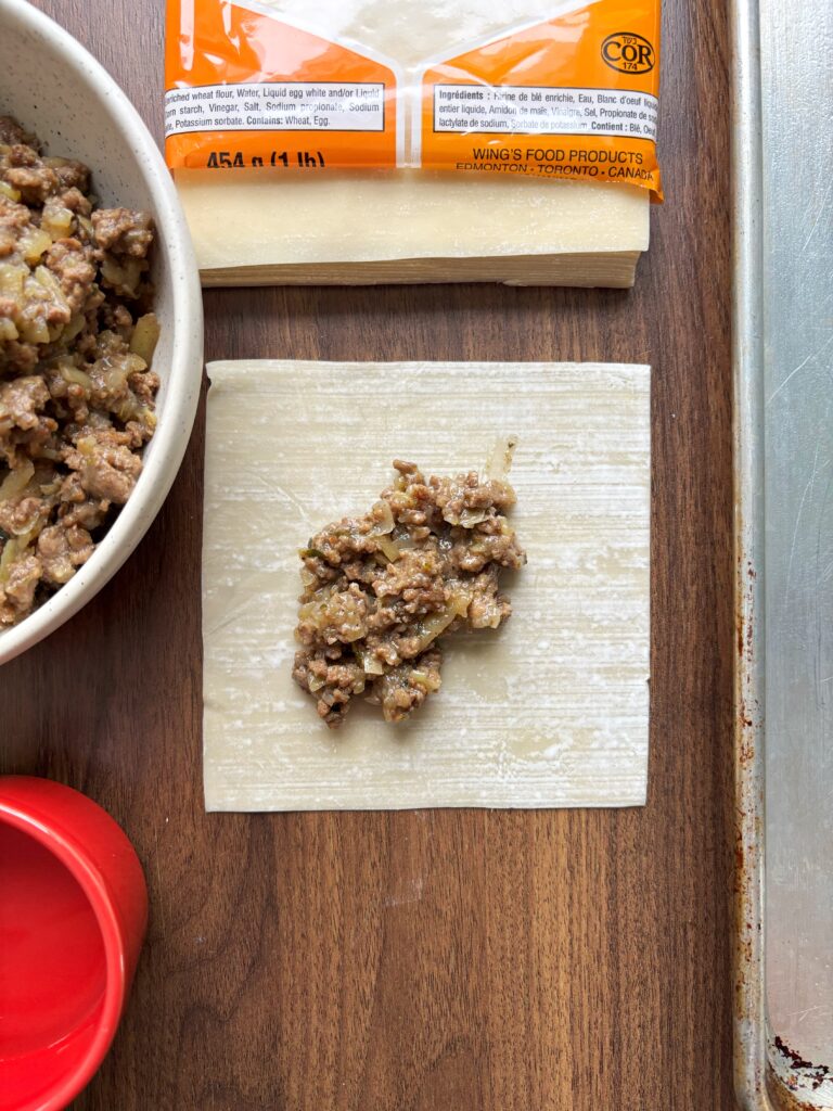 Wooden table with egg roll wrapper topped with tourtiere spring roll filling.