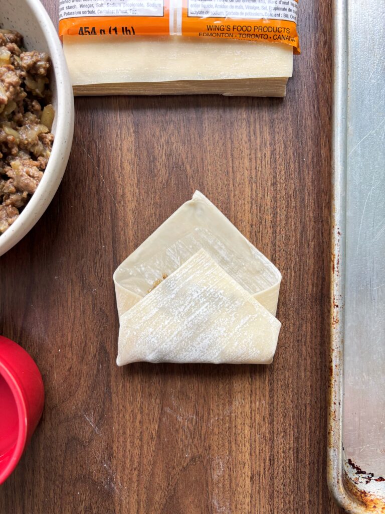 Tourtiere spring roll on a wooden table with the bottom edge folded up towards the top.