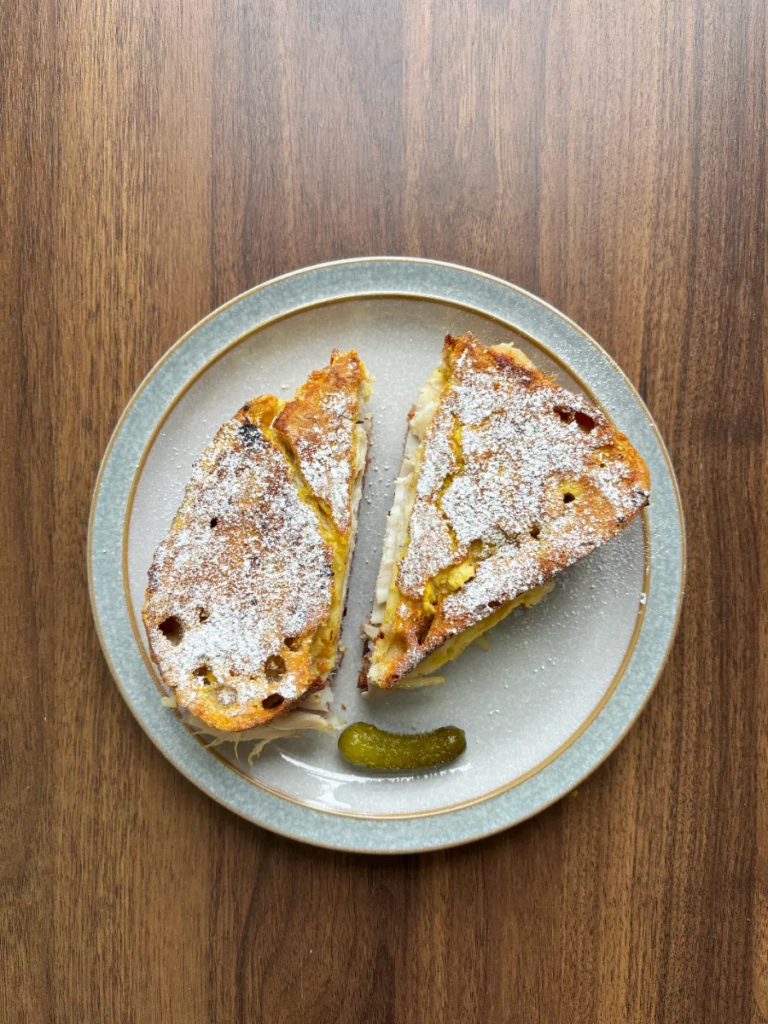 Turkey and Cherry Monte Cristo on a grey plate with a blue rim sitting on a wooden table.